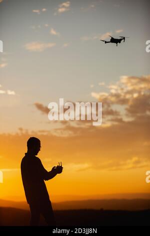 Silhouette d'un jeune homme utilisant un drone dans UN Cadre rural au coucher du soleil Banque D'Images