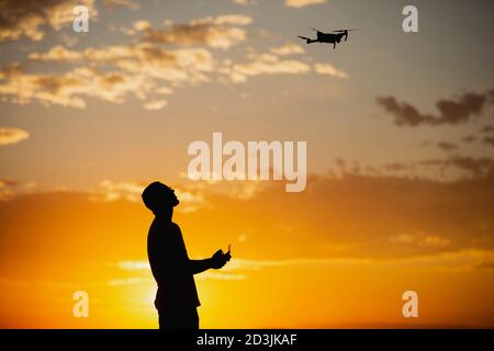 Silhouette d'un jeune homme utilisant un drone dans UN Cadre rural au coucher du soleil Banque D'Images