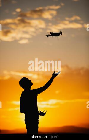Silhouette d'un jeune homme utilisant un drone dans UN Cadre rural au coucher du soleil Banque D'Images
