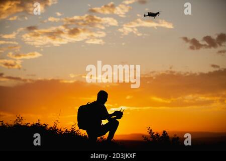 Silhouette d'un jeune homme avec un sac à dos exploitant un Drone dans UN cadre rural au coucher du soleil Banque D'Images