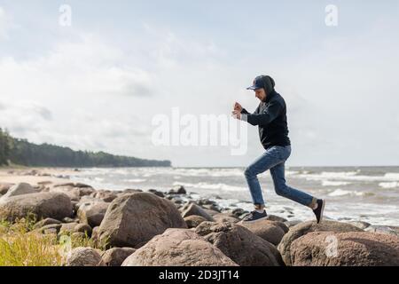 Un jeune homme s'amusant sur la plage de Baltic See, passant d'un grand rocher à l'autre Banque D'Images