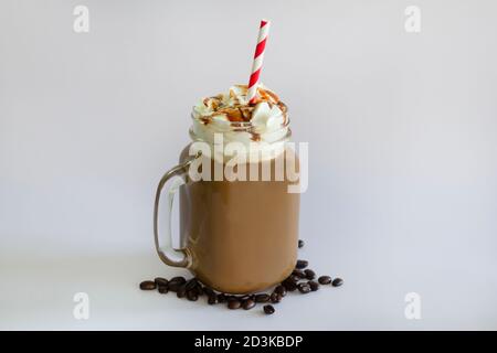 Délicieux café glacé ou Frappuccino à la crème fouettée, au sirop et à la paille rouge. Avec grains de café isolés sur fond blanc. Banque D'Images