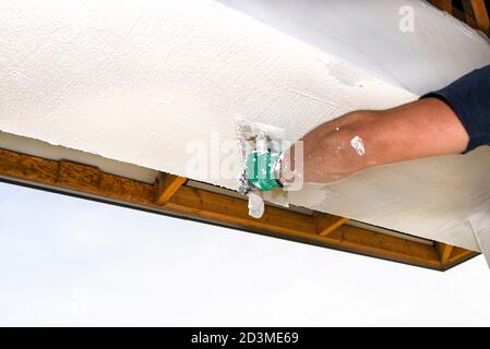 Un ouvrier de la construction applique et estompe une couche blanche de plâtre de silicone sur les façades de la maison. Banque D'Images