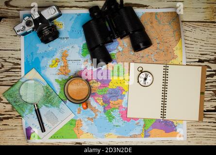 Mise à plat du concept de planification de voyage. Vue de dessus d'un agenda, de jumelles, d'une boussole, d'un appareil photo rétro, d'un café et d'une carte d'Europe sur une table en bois blanc Banque D'Images