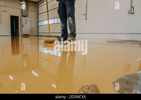 Ouvrier, revêtement de sol avec de la résine époxy auto-nivelante dans un atelier industriel. Banque D'Images