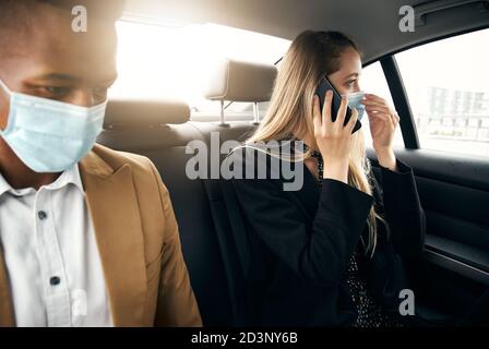 Couple d'affaires portant des masques utilisant un ordinateur portable et un téléphone mobile Retour du taxi pendant la pandémie de santé Banque D'Images