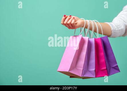 Sacs en papier de couleur sur les mains d'une femme sur un fond bleu. Une jeune femme tient sur sa main des sacs de shopping roses et violets. Banque D'Images