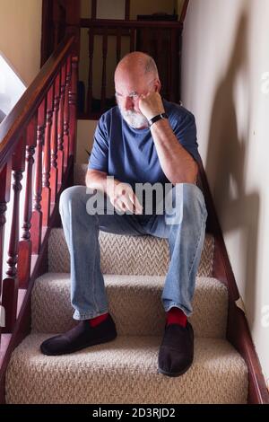 Triste, barbu homme senior assis sur les escaliers dans sa vieille maison. Banque D'Images