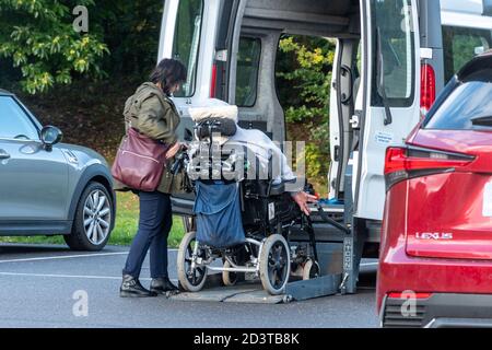 Personne à mobilité réduite et soignant utilisant l'ascenseur sur un fauteuil roulant minibus accessible Banque D'Images