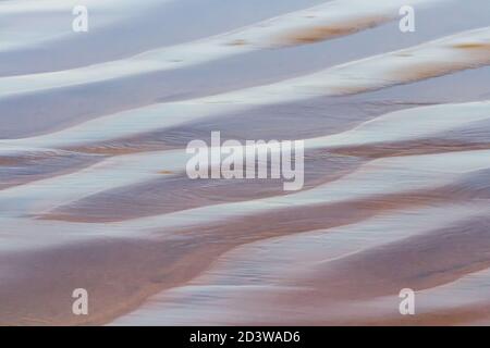 Texture de la plage - l'eau de mer repose brièvement dans des trous de sable sur son chemin vers l'océan Pacifique. Pismo Beach, Californie, États-Unis. Banque D'Images