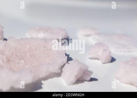 Bande de cristaux de flocons de sel blanc rose sur la surface brillante du miroir réfléchissant blanc. Station thermale, ingrédients cristallisés, vue rapprochée ensoleillée avec attention sélective Banque D'Images