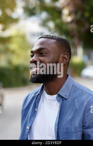 Gros plan sur un homme afro-américain heureux. Beau jeune homme en chemise bleue en denim marchant dans la rue et souriant Banque D'Images