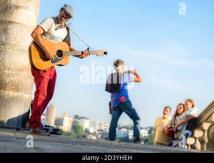 Le chanteur de rue et le guitariste sont présents dans la rue pendant que les touristes prennent des photos du paysage urbain Banque D'Images