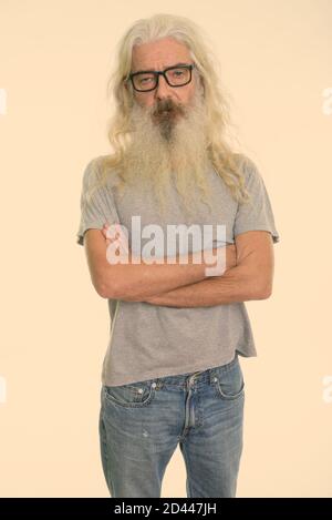 Studio shot of senior homme barbu debout tout en portant des lunettes avec les bras croisés Banque D'Images