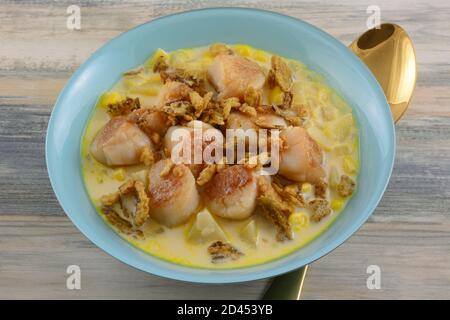 Soupe de chaudrée épicée aux noix de Saint-Jacques, aux pommes de terre et au maïs et croustillante garniture au piment jalapeno dans un bol bleu avec une cuillère à soupe dorée Banque D'Images