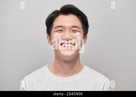 toilettage, soins de la peau et concept de personnes - jeune indien souriant appliquant de la crème au visage sur fond blanc Banque D'Images