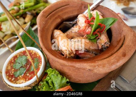 Crevettes cuites dans une marmite en argile sur une table en bois, avec une sauce épicée de fruits de mer thaïlandais, il est disposé et joliment décoré. Banque D'Images