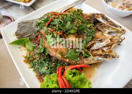 Remuez le poisson épicé frit sur une assiette blanche garnie de piment et de feuilles astringentes. Décorez le plat avec de beaux légumes, des fruits de mer thaïlandais populaires. Banque D'Images