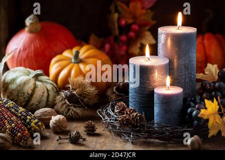 Concept de récolte d'automne ou d'automne avec bougies allumées, citrouilles décoratives, maïs, noix, raisins et pommes de pin Banque D'Images