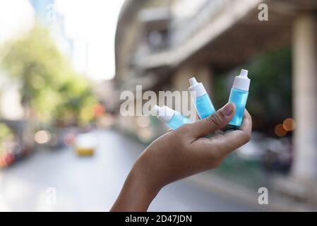 La main tenant une petite bouteille de gel pour les mains bleu d'alcool éthylique assainisseur, grande et petite taille, placez sur le mur à proximité de la jonction dans la ville, importa Banque D'Images