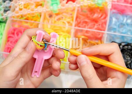 Tissage en caoutchouc. Tricoter les bandes en caoutchouc avec la maille de métier à tisser. Mains de fille tissage bracelet de bandes en caoutchouc. Banque D'Images