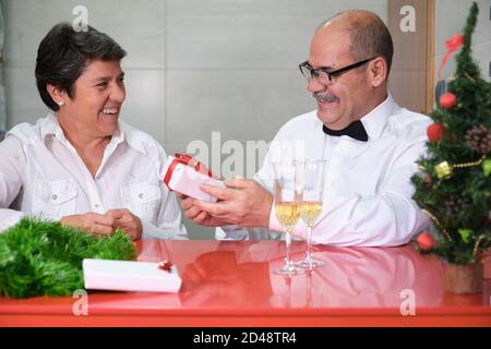 Femme donnant un cadeau à son mari. Couple senior célébrant noël. Concept de fête de Noël. Banque D'Images