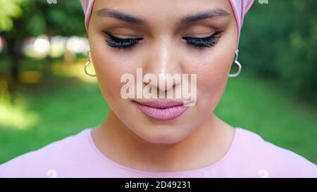 femme tendance avec boucles d'oreilles argentées et hijab violet avec fermé les yeux se trouvent contre les gros plan du parc Banque D'Images