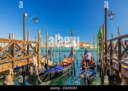 Gondoles amarrées à une jetée en bois dans l'eau du bassin de San Marco. Île de San Giorgio Maggiore avec Campanile San Giorgio dans la lagune vénitienne, ciel bleu clair, ville de Venise, région de Vénétie, Italie Banque D'Images