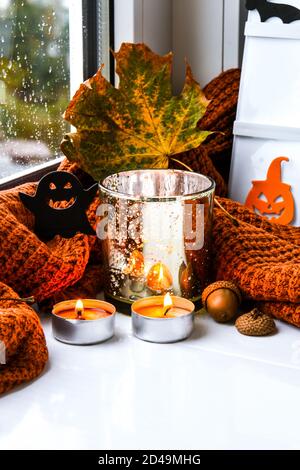 Bougies avec chandail et potiron fantôme, feuilles séchées sur le rebord de la fenêtre. Décoration de la maison d'Halloween. Fenêtre de pluie. Banque D'Images