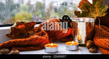 Bougies avec chandail et potiron fantôme, feuilles séchées sur le rebord de la fenêtre. Décoration de la maison d'Halloween. Fenêtre de pluie. Banque D'Images