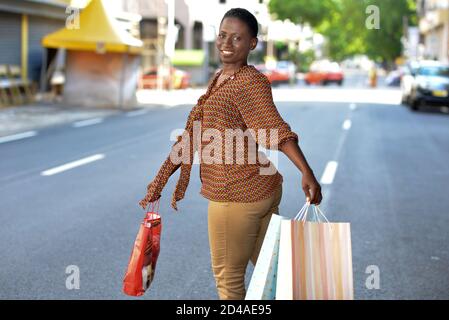 Une jeune femme se réjouit de ses achats en tenant une pile de sacs en papier dans la rue. Concepts d'offre de vente à prix réduit rentable Banque D'Images