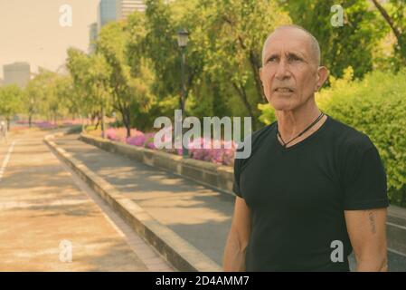 Senior homme chauve touristique pensée sur le côté de la rue au parc paisible à Bangkok en Thaïlande Banque D'Images