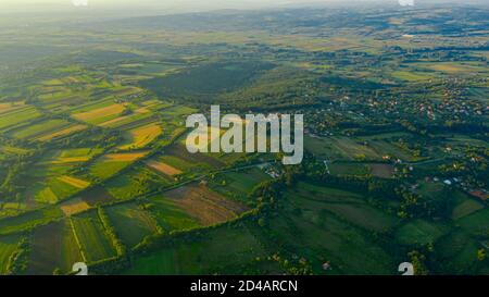 Photographié au-dessus de paysage vert vallonné, plusieurs parcelles cultivées parmi les arbres forestiers et la ville au loin. Banque D'Images