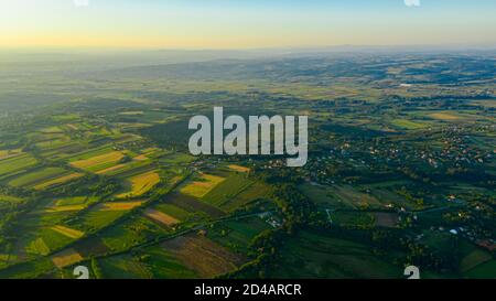 Photographié au-dessus de paysage vert vallonné, plusieurs parcelles cultivées parmi les arbres forestiers et la ville au loin. Banque D'Images