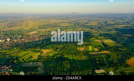 Photographié au-dessus de paysage vert vallonné, plusieurs parcelles cultivées parmi les arbres forestiers et la ville au loin. Banque D'Images