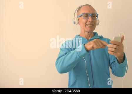 Photo en studio d'un homme âgé chauve heureux utilisant un téléphone portable et écouter de la musique avec des lunettes Banque D'Images