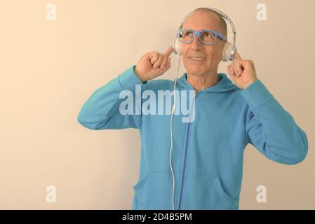 Photo en studio d'un homme âgé chauve souriant écouter de la musique et porter des lunettes Banque D'Images