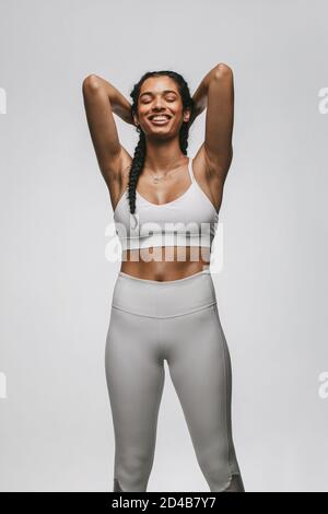 Femme en forme de sport porter debout sur fond blanc se détendre après l'entraînement. Femme en forme de sourire debout avec les mains derrière la tête. Banque D'Images