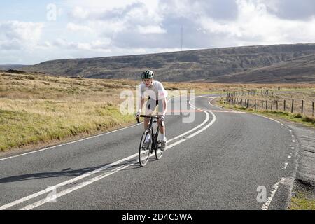 Jeune cycliste sorti de la selle en montant volontairement un Gradient sur une route Yorkshire Moors avec Holme Moss In l'arrière-plan Banque D'Images