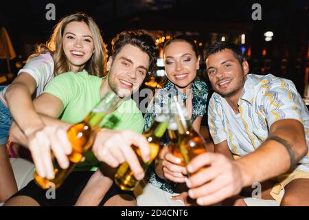 Objectif sélectif de jeunes amis se clinquant avec de la bière à l'extérieur à nuit Banque D'Images