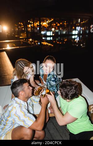 Des jeunes amis se sont servis de bouteilles de bière près de la piscine à nuit Banque D'Images