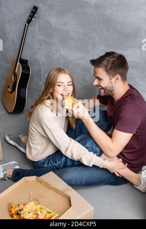 joyeux homme nourrissant votre petite amie avec une pizza près des boîtes en carton, concept mobile Banque D'Images