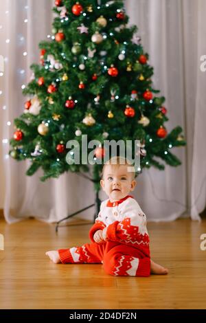 Bébé dans une combinaison tricotée rouge et blanc devant D'un arbre de Noël Banque D'Images