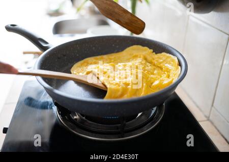 chef cuisant omelette dans une poêle chaude sur une cuisinière en bois spatule Banque D'Images