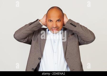 Homme contrarié homme d'affaires afro-américain en veste, couvrant ses oreilles avec les mains, entendre un bruit gênant, il a des maux de tête, posant pour la caméra et couvrant ses oreilles en raison du bruit. Banque D'Images