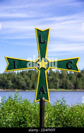 Ancienne croix de fer historique patée au symbolisme masonique dans un bosquet en face du château de Läckö sur le lac Vänern, Västergötland, Suède. Banque D'Images