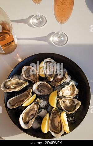 Huîtres fraîches avec citron et deux verres de vin mousseux rose. Fruits de mer sur table wjite. Banque D'Images