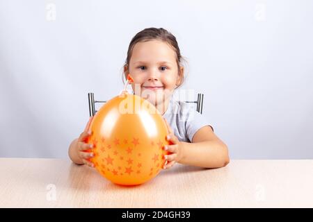 fille souriante tenant un ballon orange et assis à un tableau sur fond gris Banque D'Images