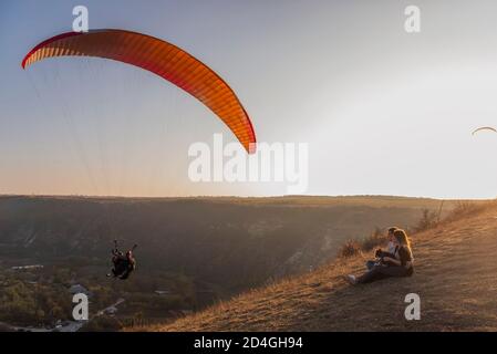 Assis sur un canyon, regardant les parapentes volant dans le ciel au coucher du soleil. Voyage avec les animaux de compagnie. Jeune famille avec un voyage en chien schnauzer. Moldavie, ancienne Orhey Banque D'Images