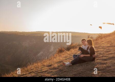 Assis sur un canyon, regardant les parapentes volant dans le ciel au coucher du soleil. Voyage avec les animaux de compagnie. Jeune famille avec un voyage en chien schnauzer. Moldavie, ancienne Orhey Banque D'Images